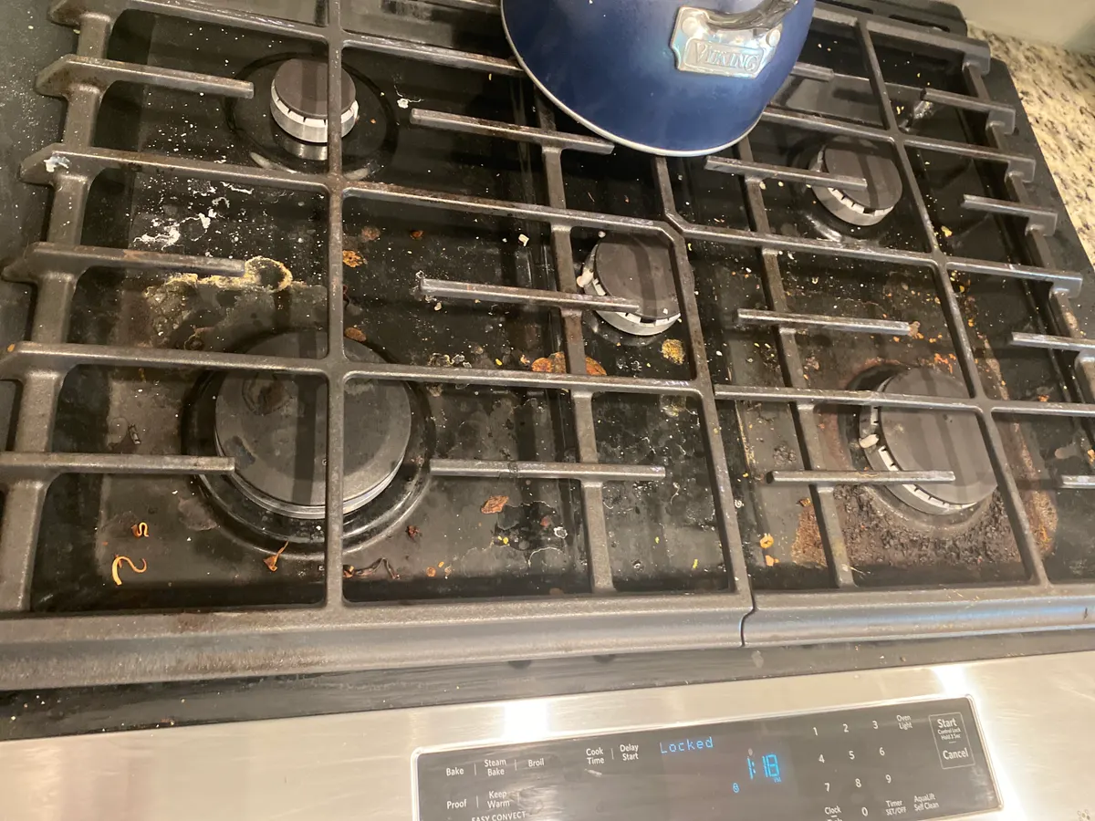 Gas stovetop before cleaning, with crumbs and spills around the burners
